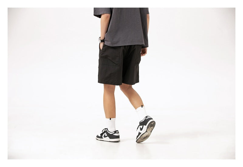 Rear three-quarter view of a model wearing black shorts with a dark gray T-shirt and sneakers.