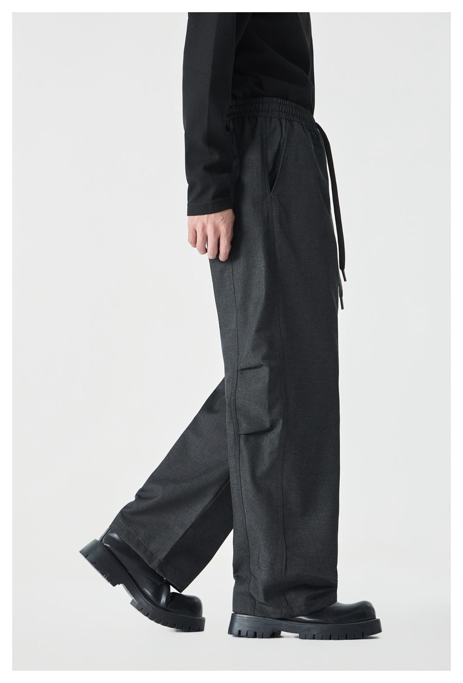 Side view of a model wearing charcoal wide-leg drawstring pants with black shoes.