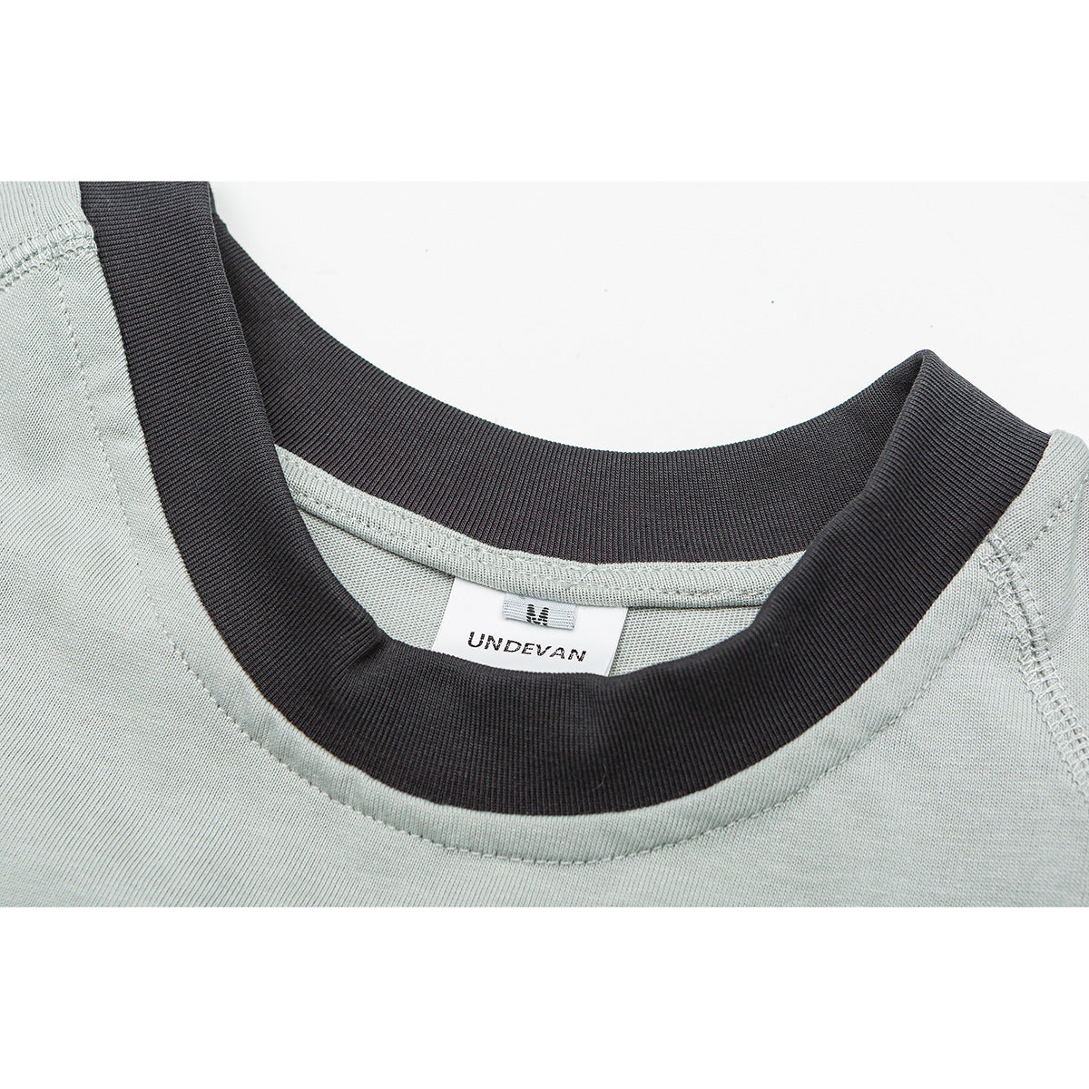 Close-up of a pale sage shirt with a dark ribbed crew neck and a visible UNDEVAN neck label.