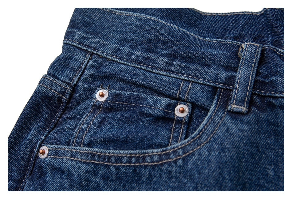 Close-up of a dark blue jeans front pocket, coin pocket, and metal rivets.