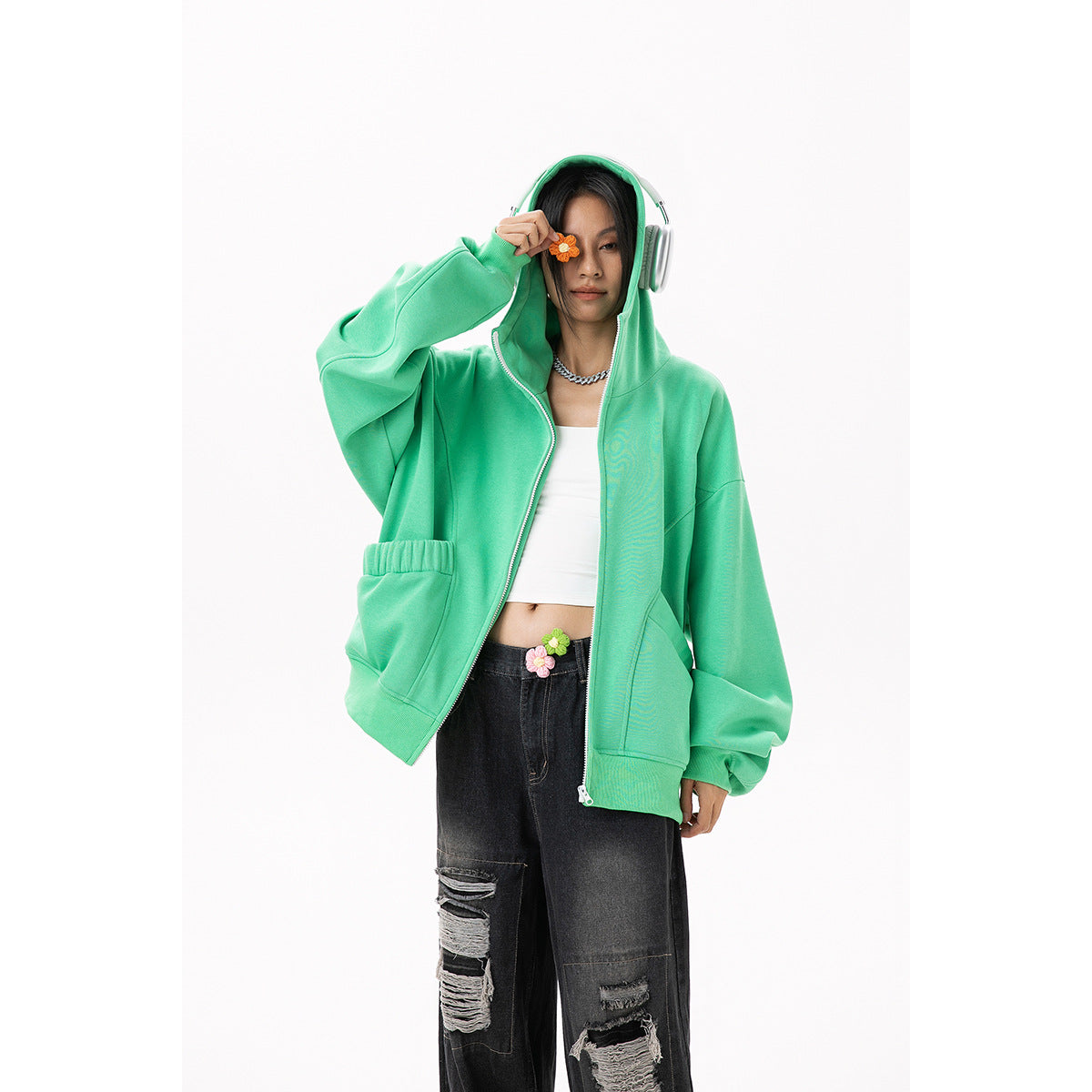 Model in a mint-green floral-appliqué hoodie and ripped black jeans, holding an orange flower near her eye.