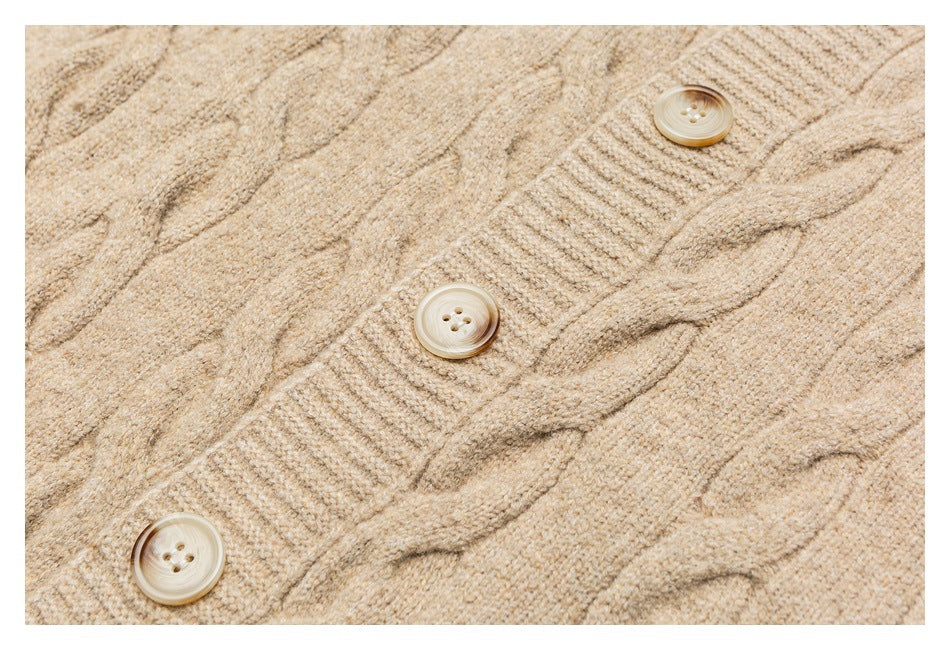 Close-up of beige cable-knit cardigan fabric, showing the cable pattern and three buttons.