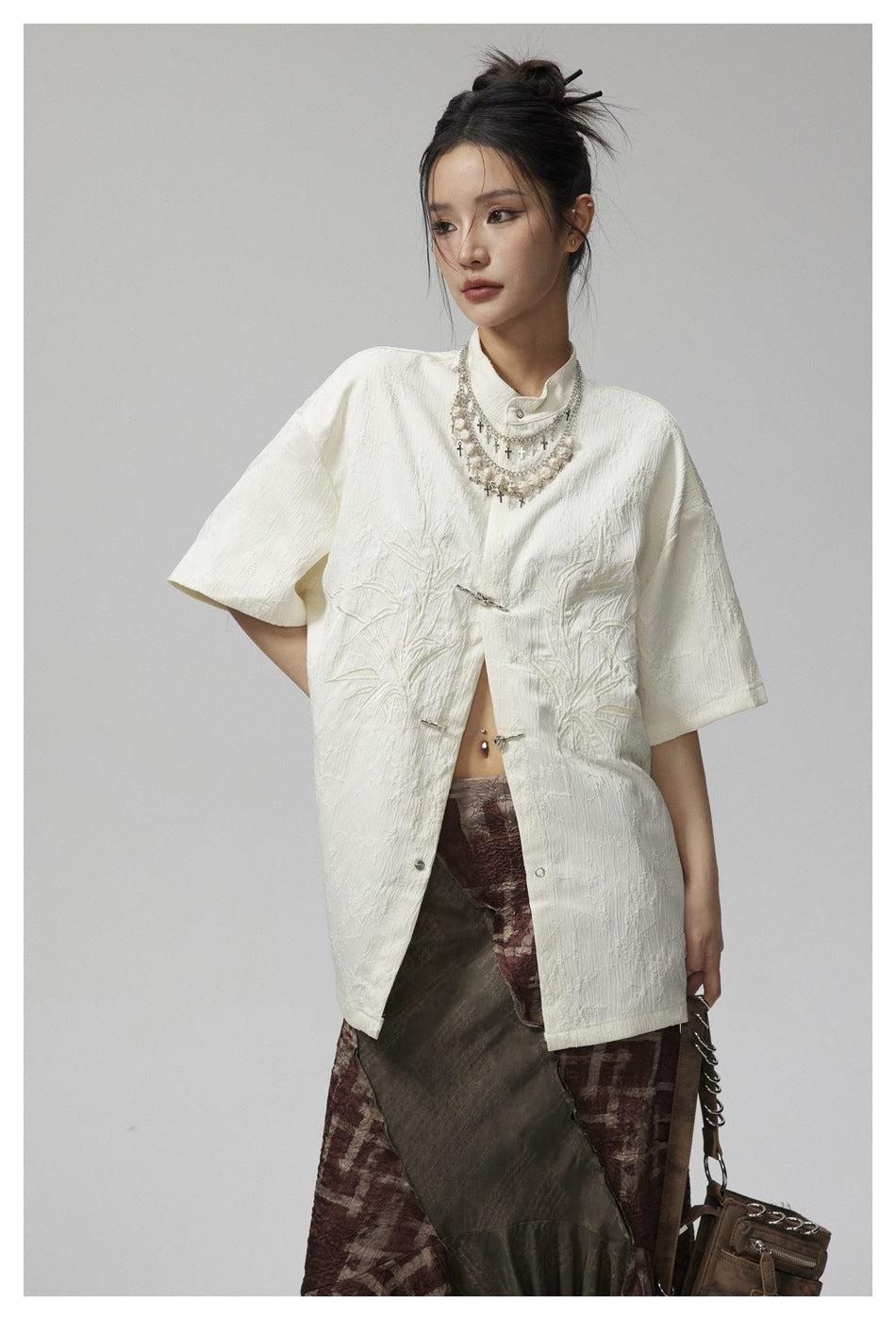 Model wearing an ivory oversized short-sleeve jacket with a stand collar, metal frog closures and raised botanical