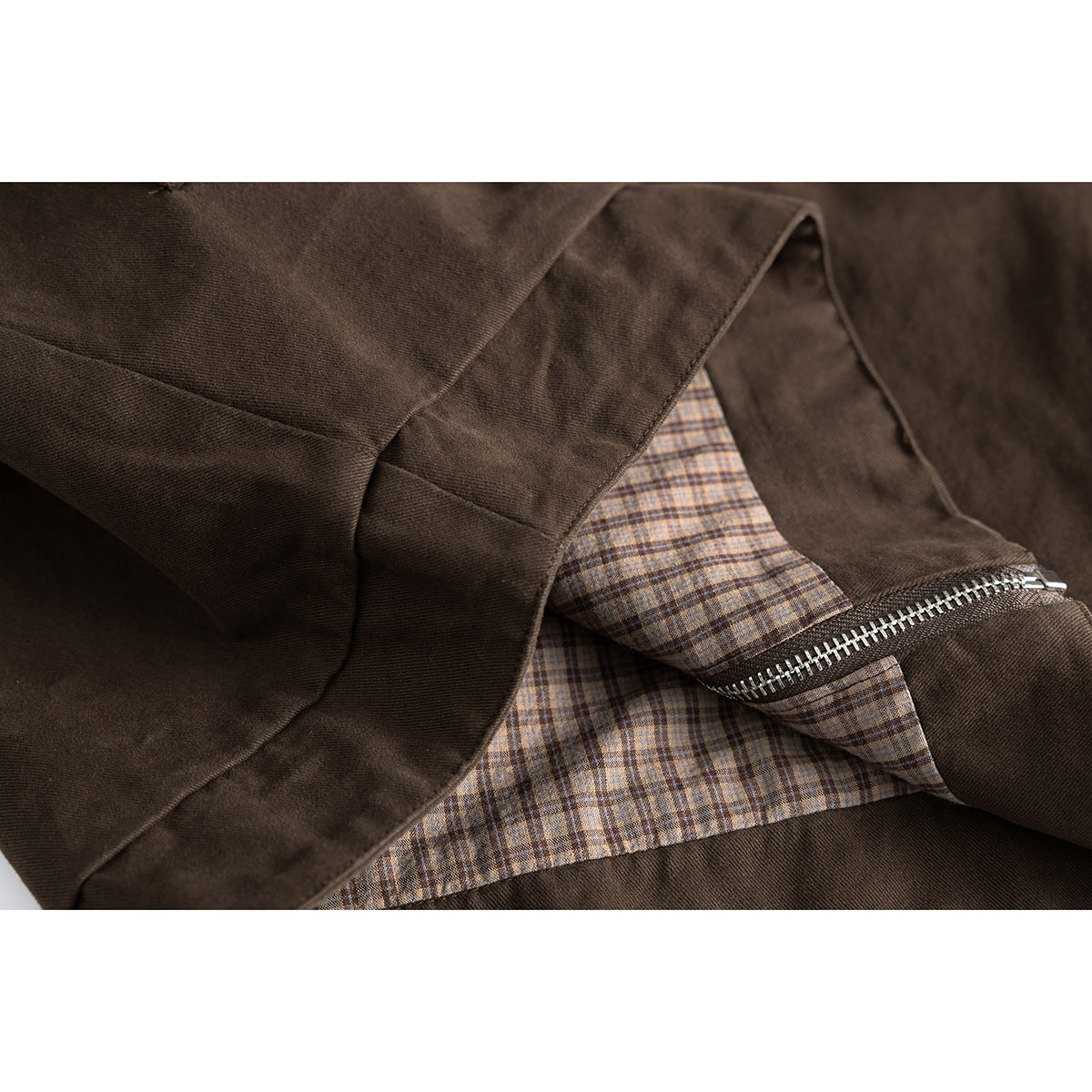 Close-up of a dark brown jacket opened to show its brown checked lining and silver zipper.