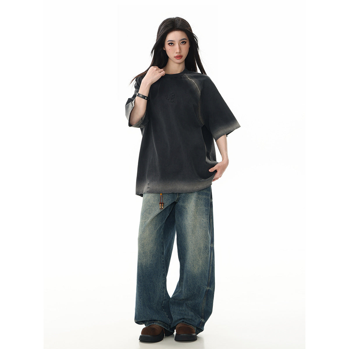 Model wearing an oversized charcoal T-shirt with faded gray accents, paired with wide-leg blue jeans.