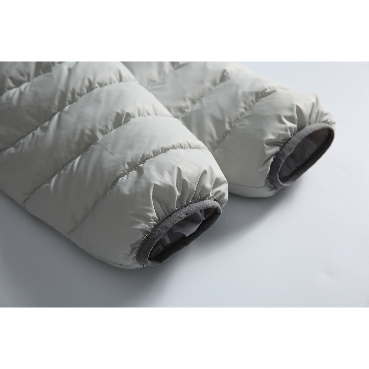 Close-up of the padded sleeves and dark gray-trimmed cuffs of a light gray puffer jacket.
