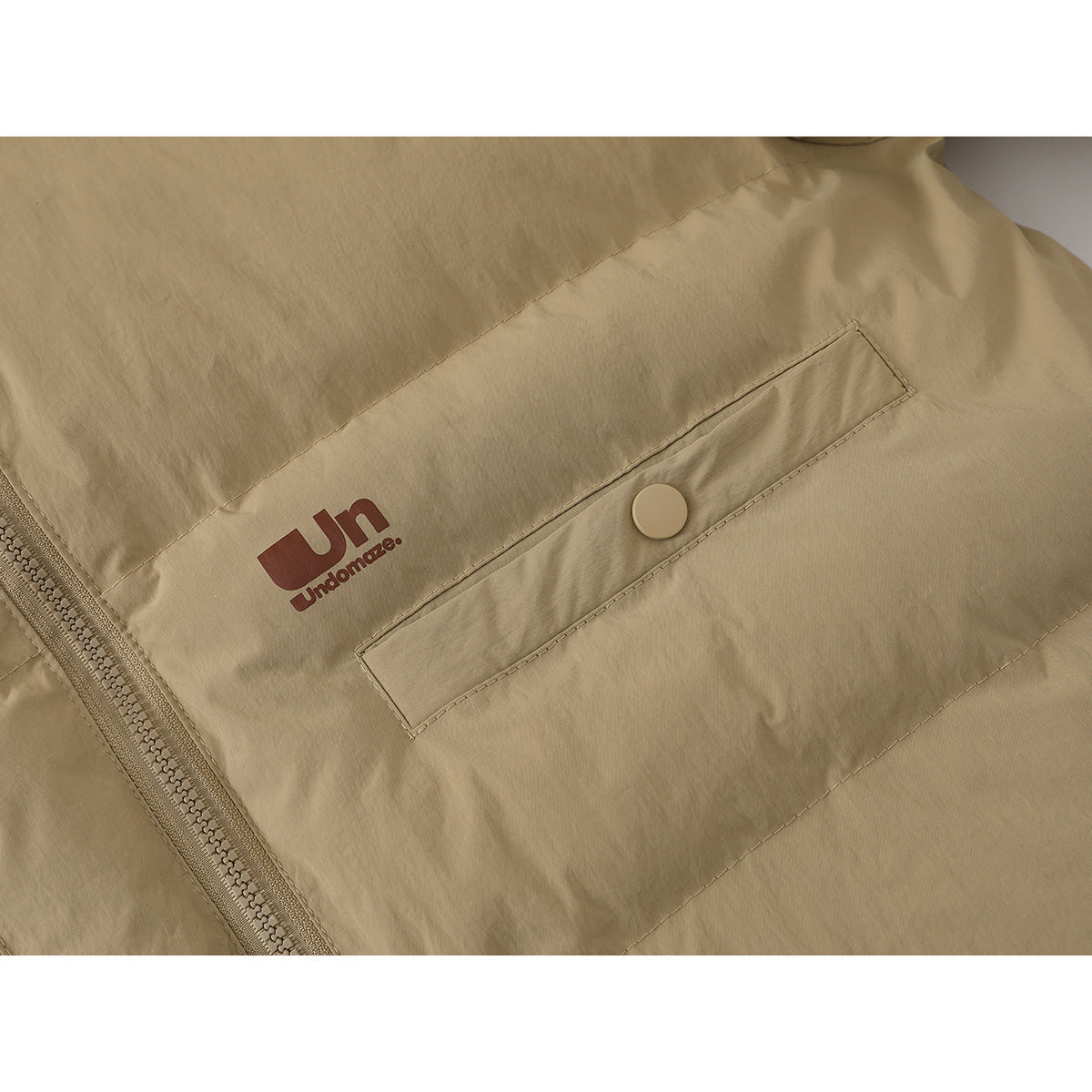 Close-up of a tan padded jacket's zippered front and snap-button pocket, with a small brown chest logo.