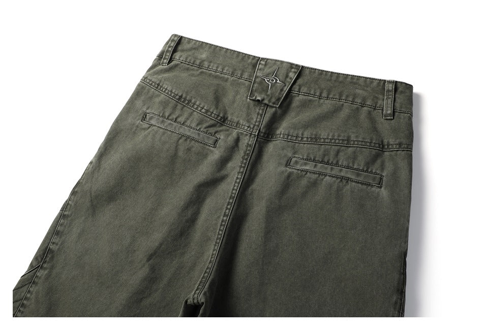Back view of dark olive-gray pants with belt loops, two welt pockets, and a small embroidered waistband emblem.