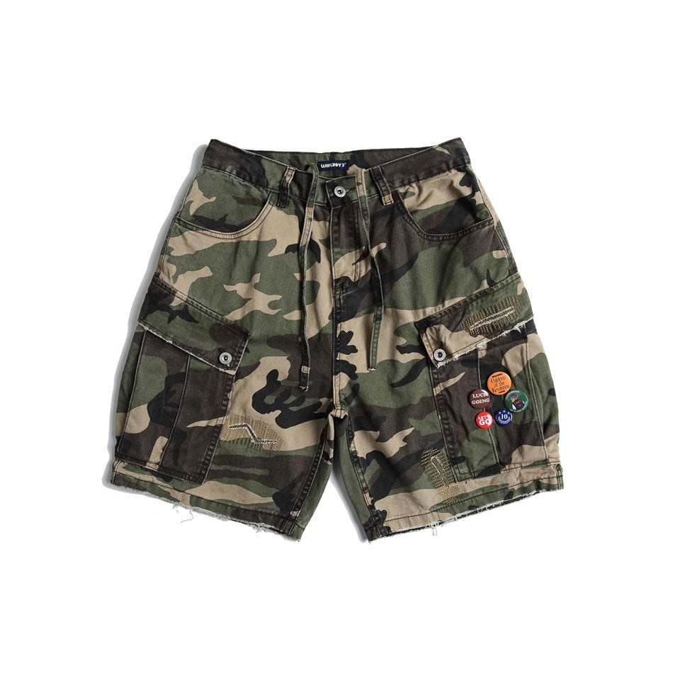 Front of camouflage cargo shorts with flap pockets, drawcord, frayed hem and small pin badges on one pocket