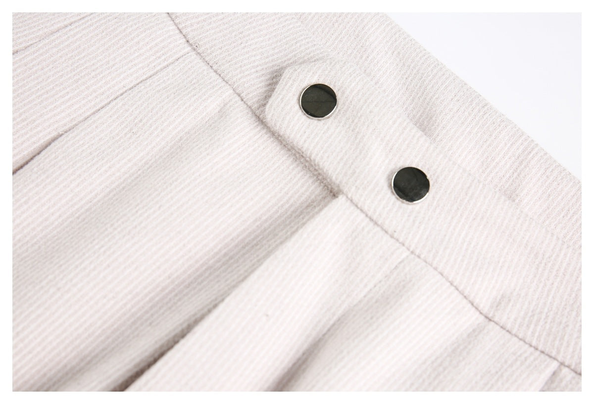 Close-up of pale beige ribbed trousers showing two dark metal waistband buttons.