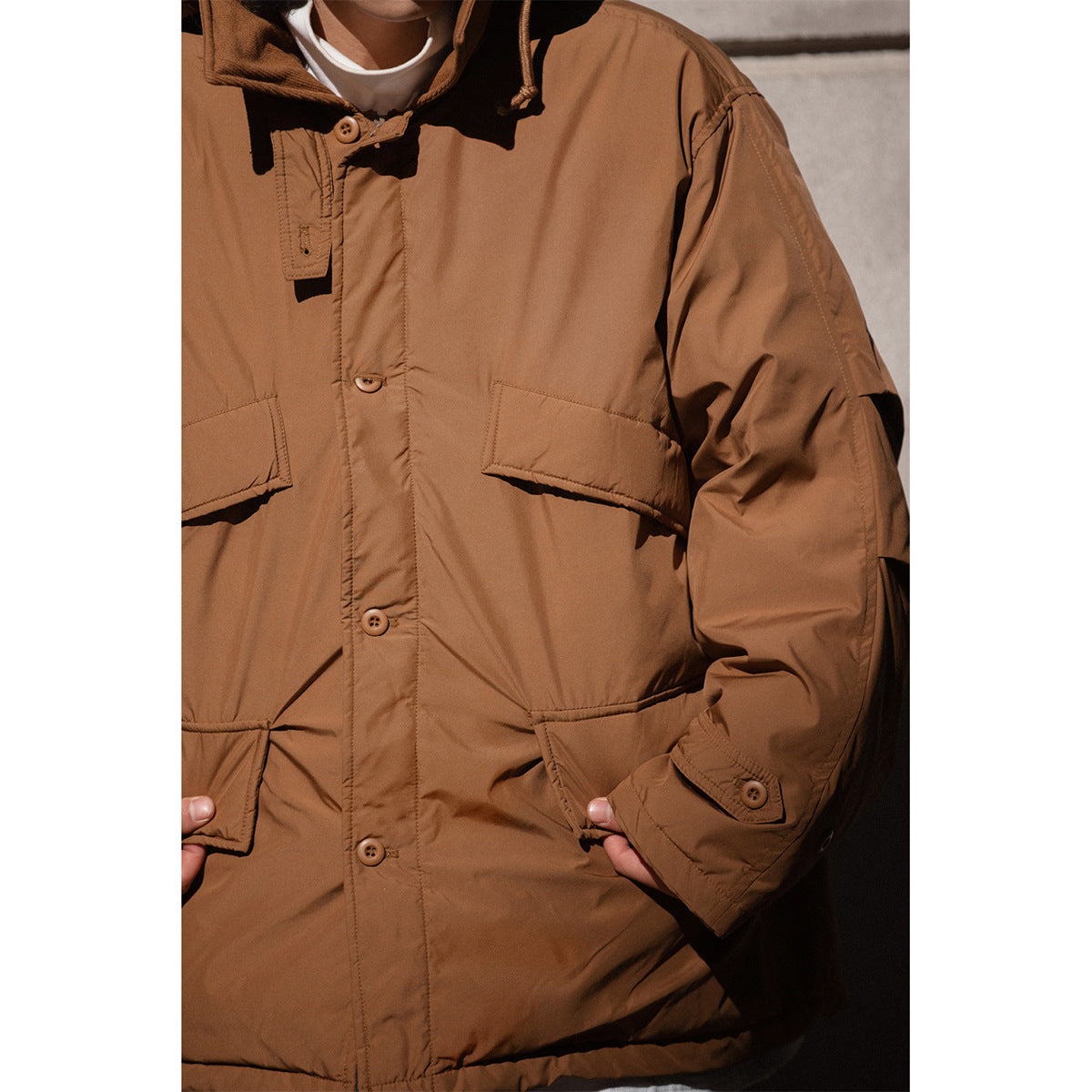 Close-up of the brown jacket showing its button placket, flap pockets, hood drawcord, and buttoned sleeve cuff.