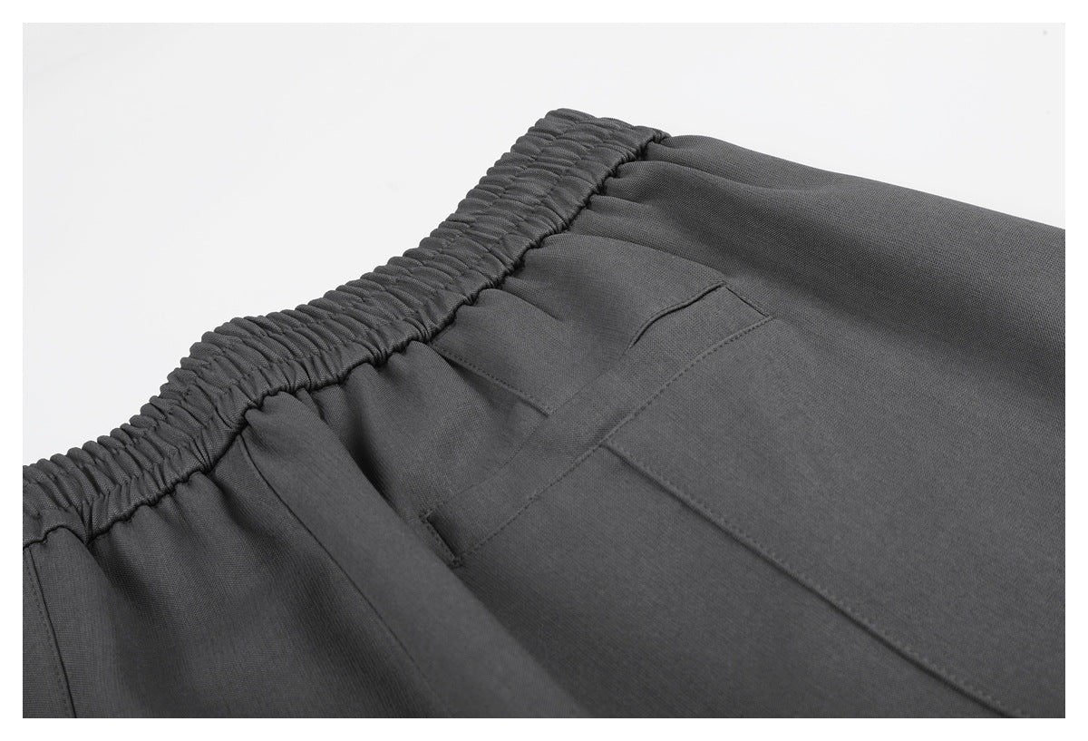 Close-up of the gathered waistband and stitched pocket on charcoal gray pants.
