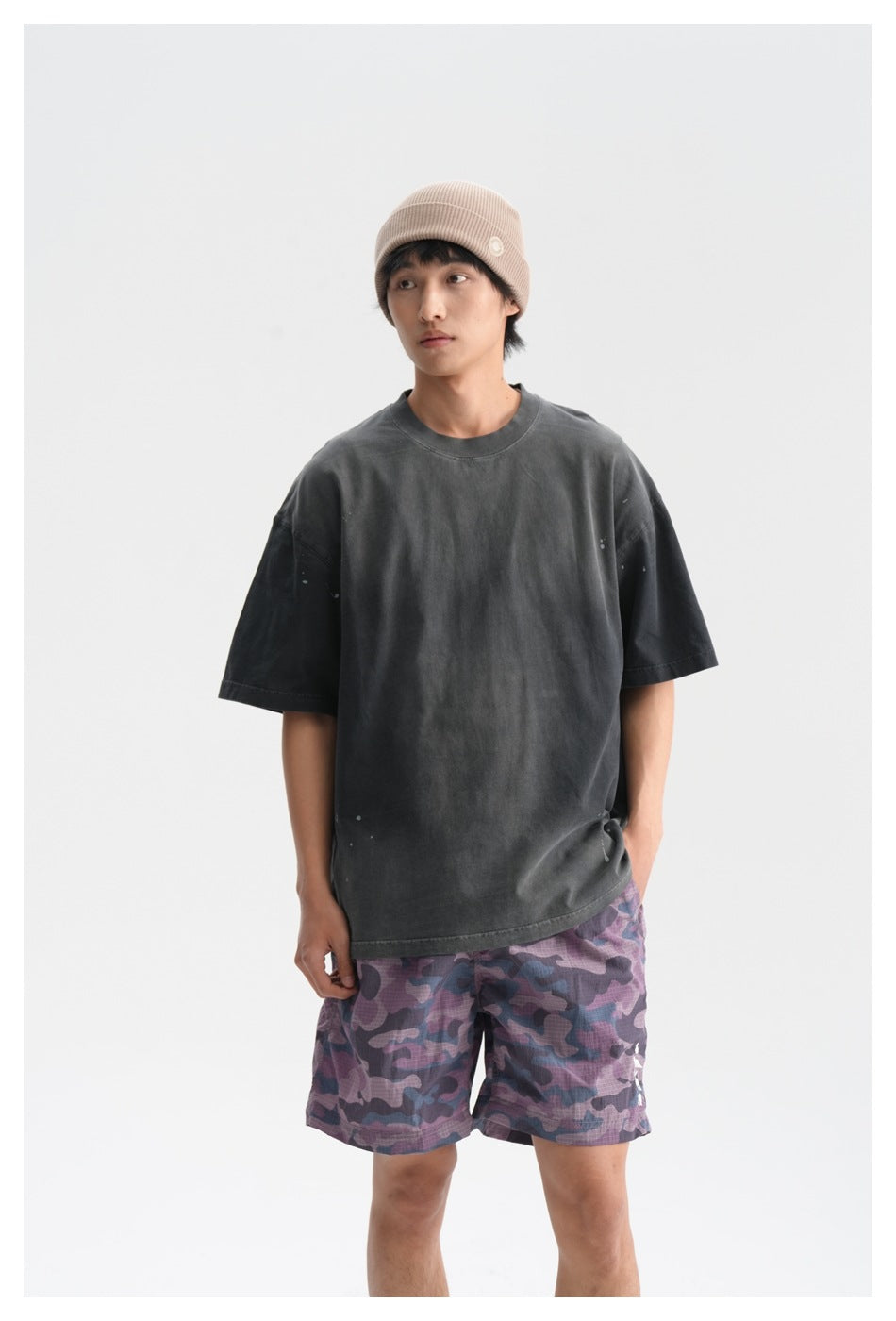 Closer front view of a model wearing a charcoal oversized T-shirt and purple camouflage shorts.