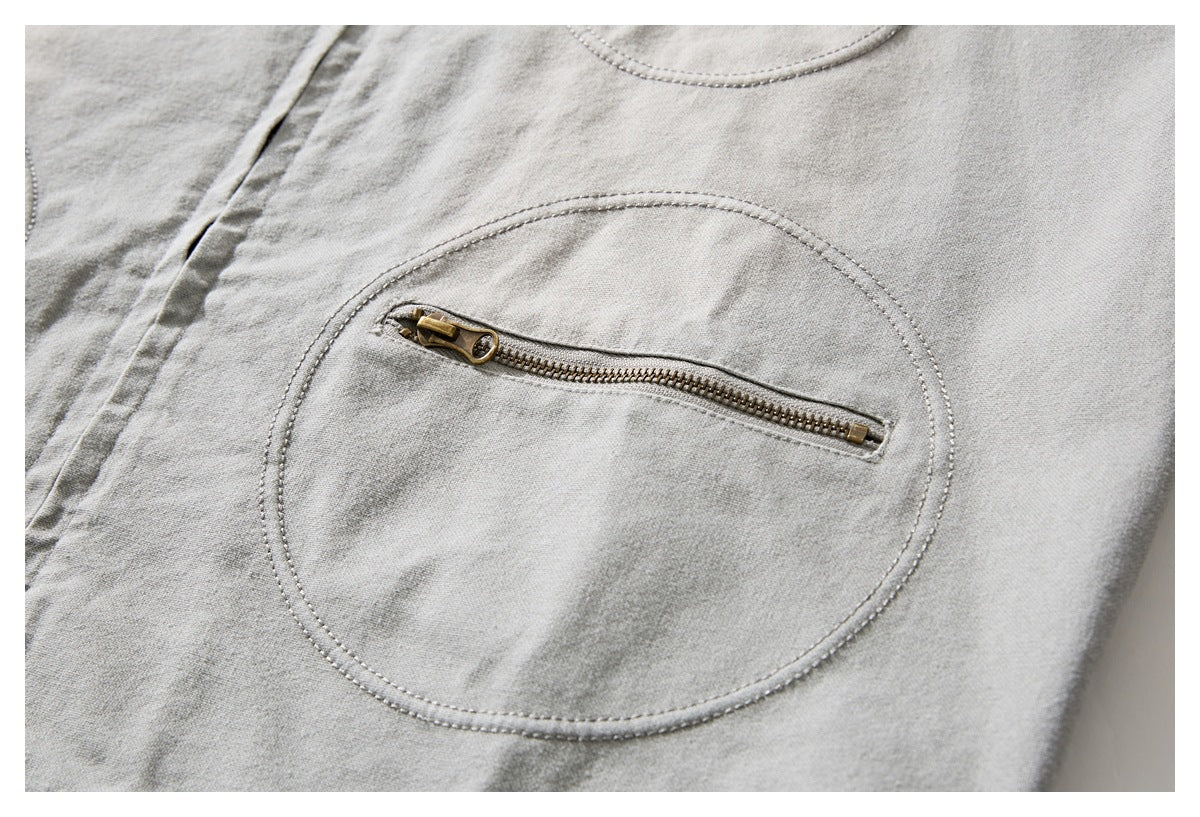 Close-up of a rounded stitched pocket with a brass zipper on a light gray jacket.