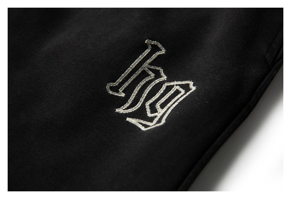 Close-up of a small cream embroidered emblem on black jogger pants.