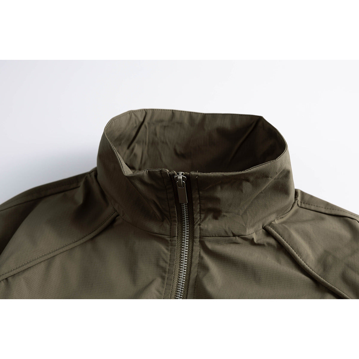 Close-up of an olive jacket's high stand collar, centered zipper, and angled shoulder seams.
