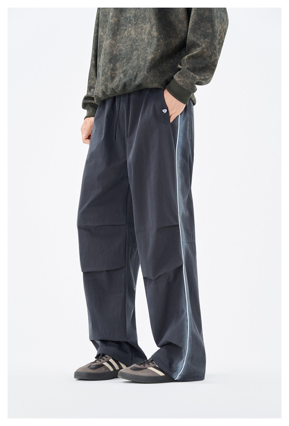 Front angle of a model wearing loose navy pants with a drawstring waist, paneled legs, and light contrast piping.