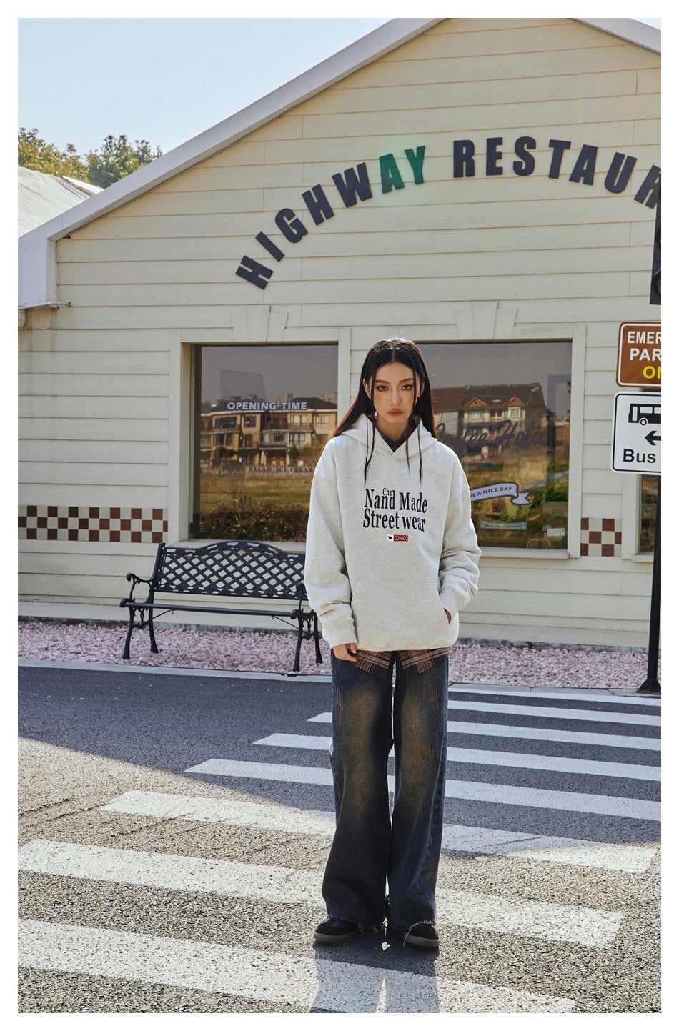 Full-length view of a model wearing a light gray graphic hoodie with loose dark jeans outdoors.