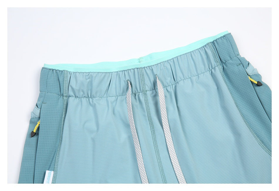 Close-up of aqua athletic shorts showing the elastic waistband, white drawcords, and side pocket details.