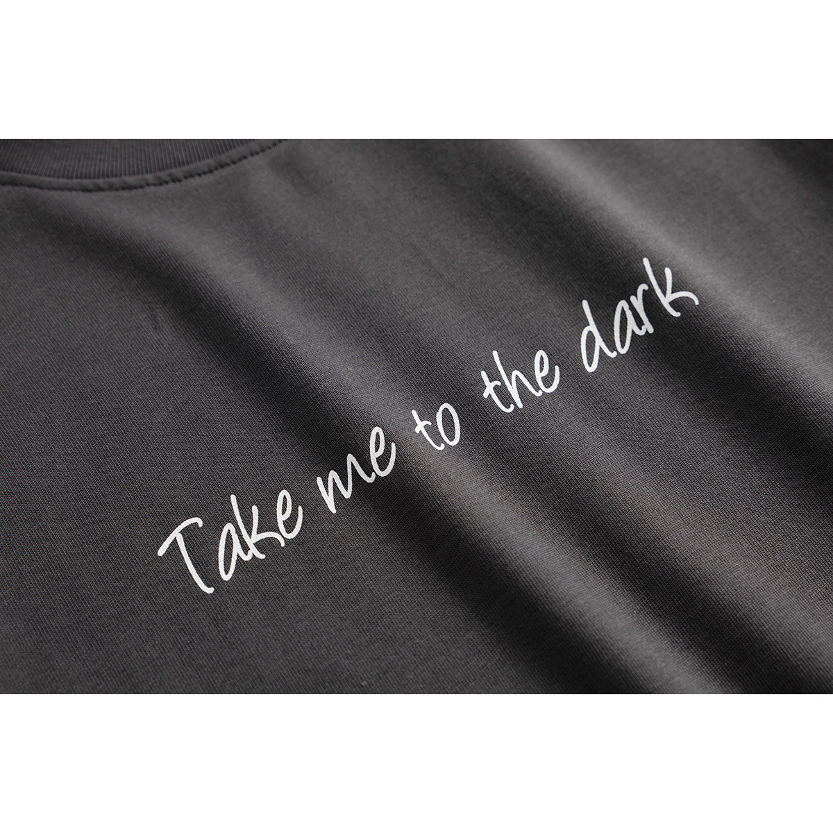 Close-up of white script reading “Take me to the dark” printed on charcoal T-shirt fabric.