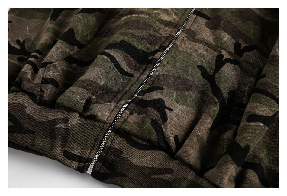 Close-up of a camouflage hoodie's front zipper, pockets, and ribbed hem.