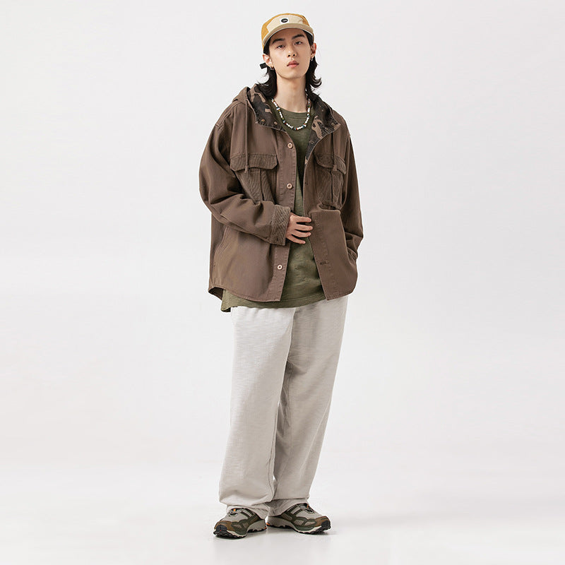 Model wearing a brown button-front utility jacket with flap pockets, an olive shirt, and loose light gray pants.
