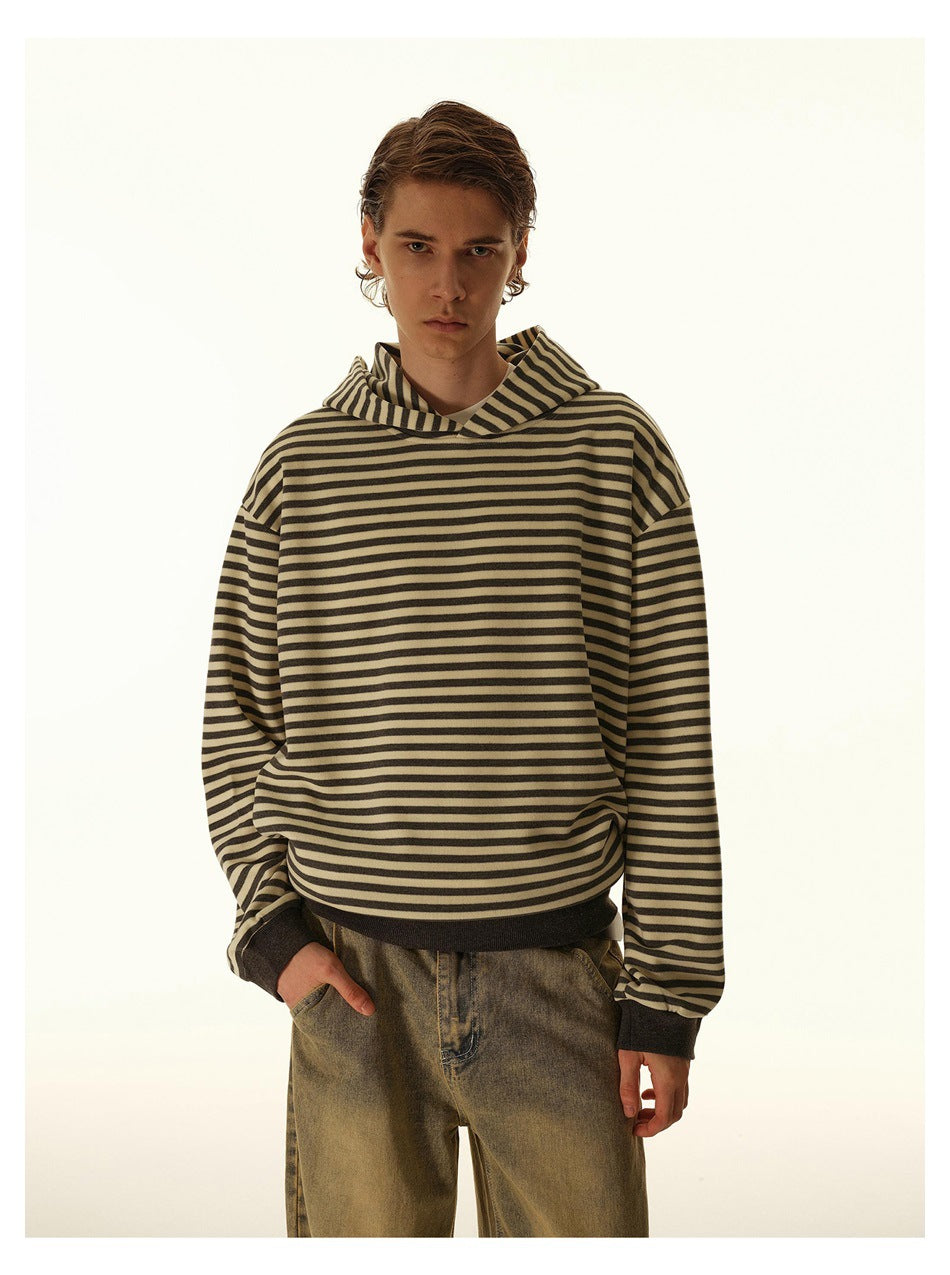 Closer view of a model wearing a tan and dark horizontal-striped hoodie with a hood and dark ribbed cuffs and hem.
