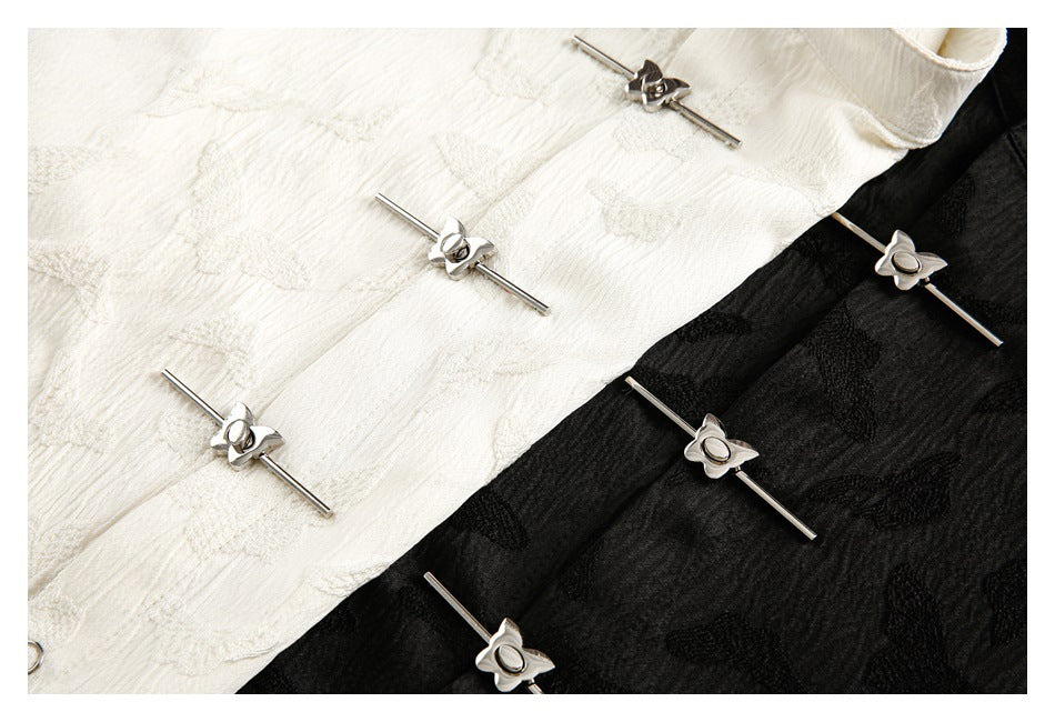 Close-up of ivory and black raised-pattern shirt fabric with slim silver bar-and-flower fasteners.