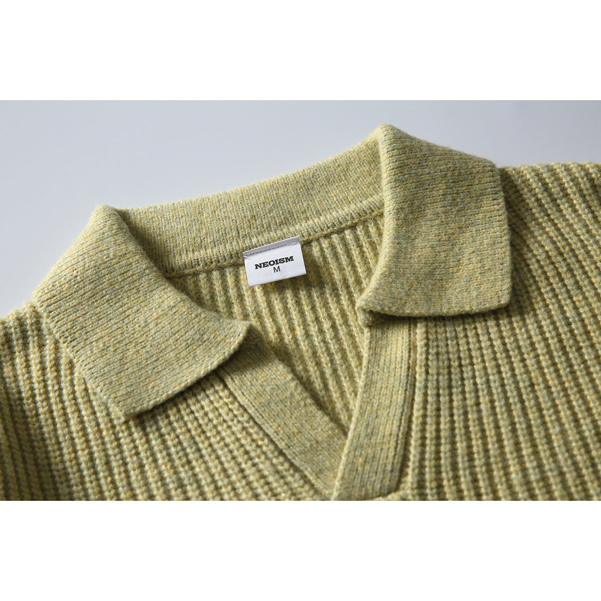 Close-up of a muted olive knit sweater showing its ribbed polo collar, V-neck opening, and inner neck label.