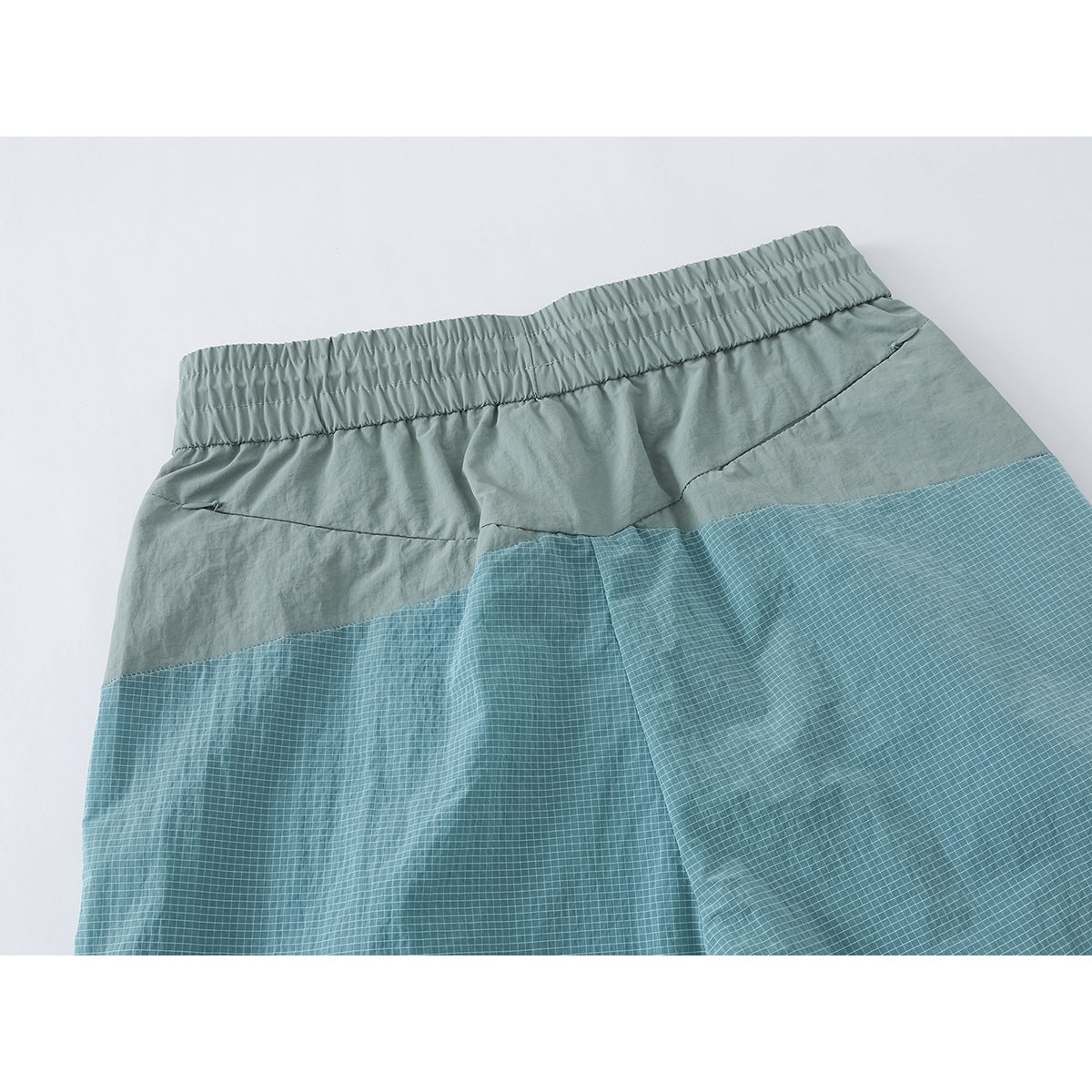 Close-up of the back of pale sage pants, with a gathered waistband and blue grid-patterned panels across the lower seat.