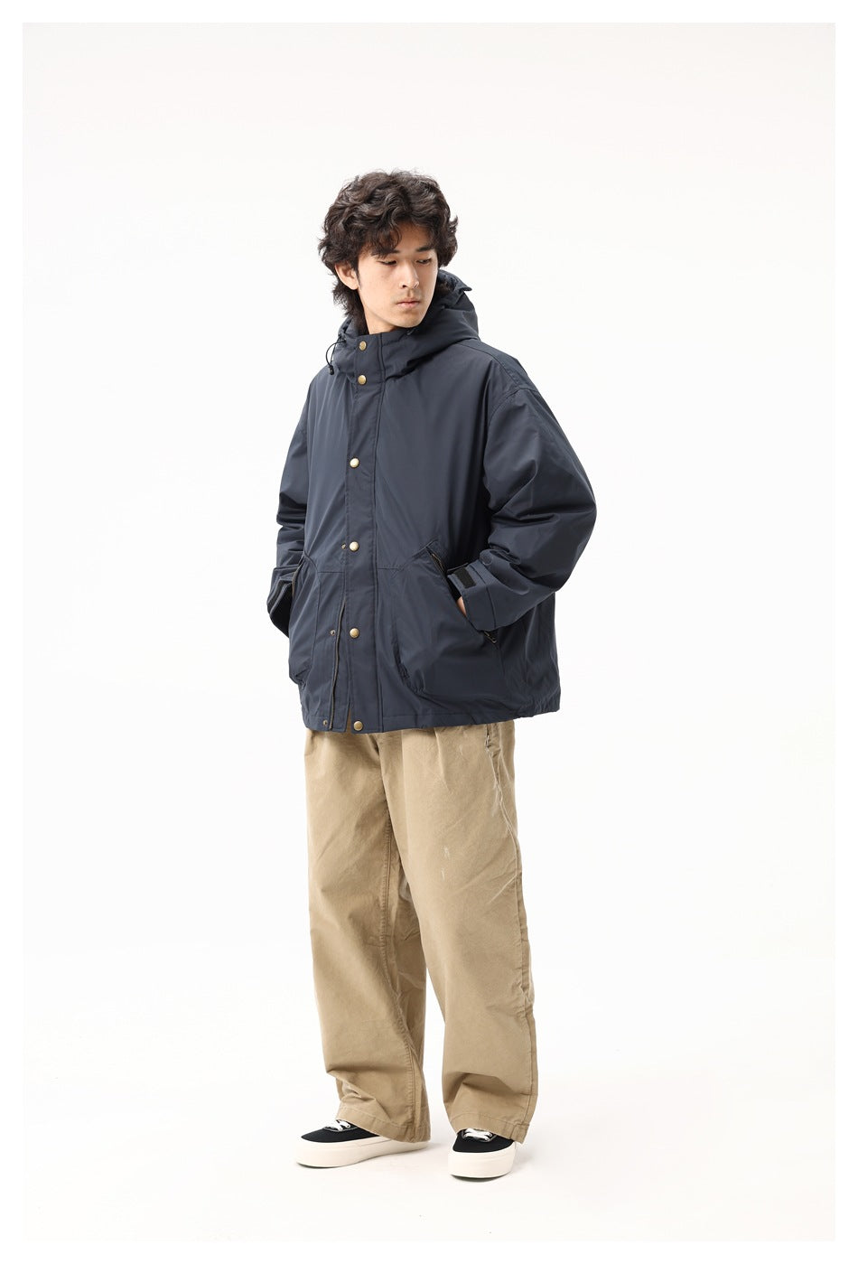 Model wearing the navy hooded jacket with wide khaki trousers and black sneakers, hand in pocket