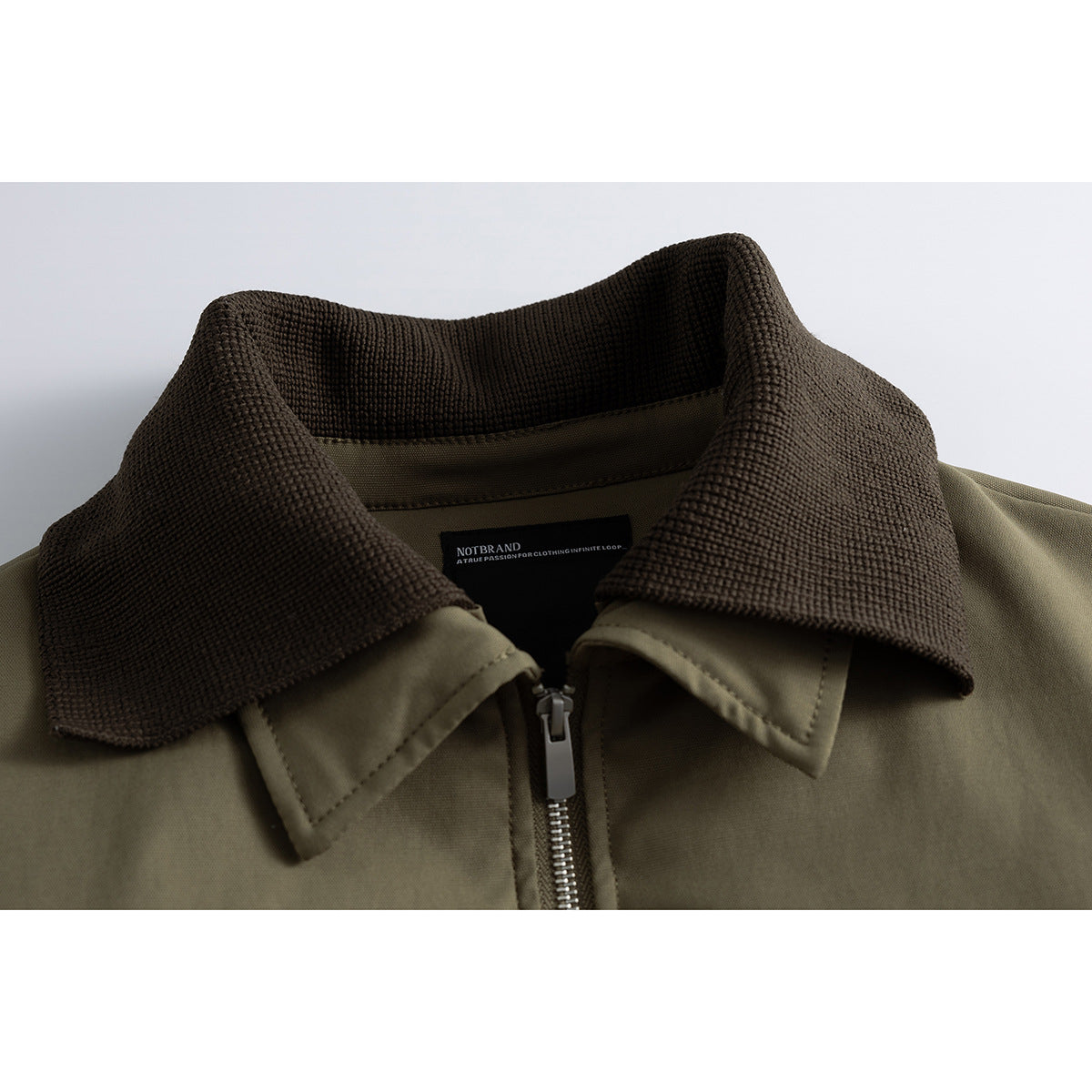 Close-up of an olive jacket with a dark brown textured collar and front zipper.