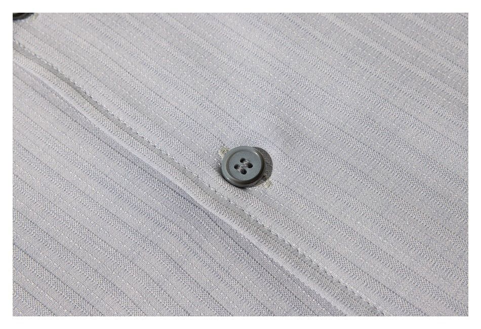 Close-up of a dark four-hole button on light gray fabric with fine diagonal stripes.