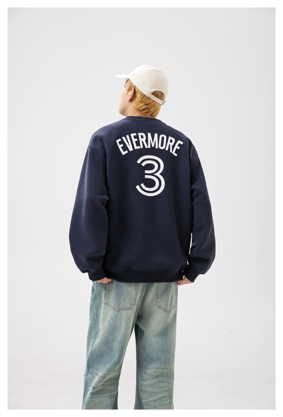 Back view of a model wearing a navy sweatshirt printed with white “EVERMORE” lettering and a large number 3.
