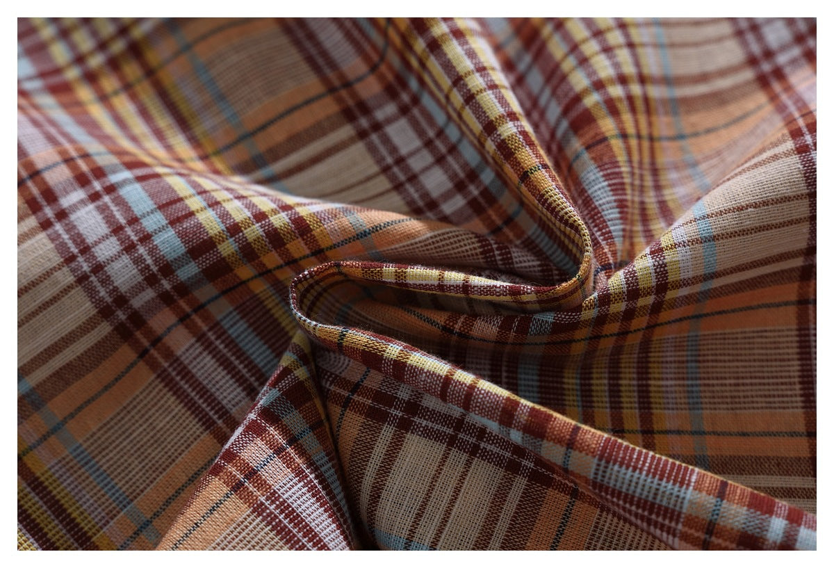 Close-up of draped plaid fabric in rust, cream, mustard, and blue, showing its woven pattern.