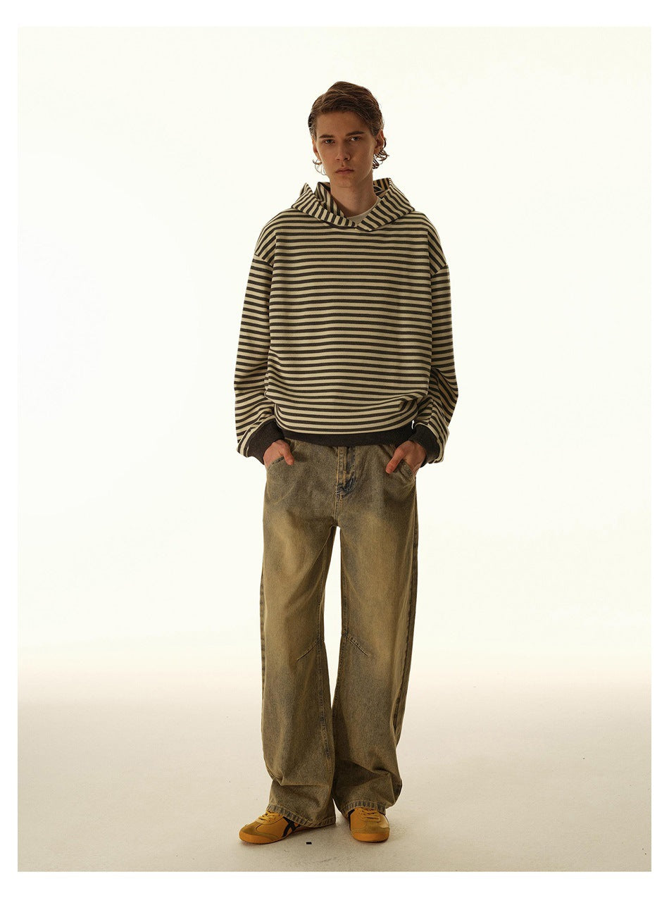 Front view of a model wearing a loose cream hoodie with dark horizontal stripes and wide-leg olive jeans.