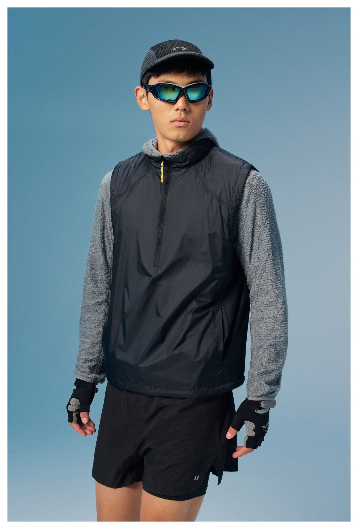 A model wears a black sleeveless zip-neck pullover over a gray textured long-sleeve top.