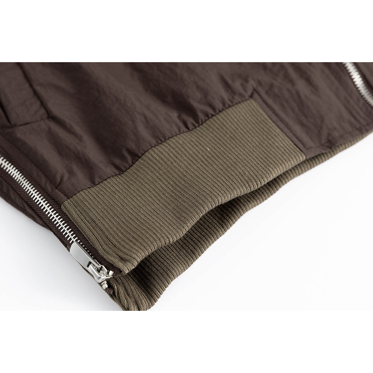Close-up of a dark brown jacket hem with olive ribbed trim and a silver zipper.