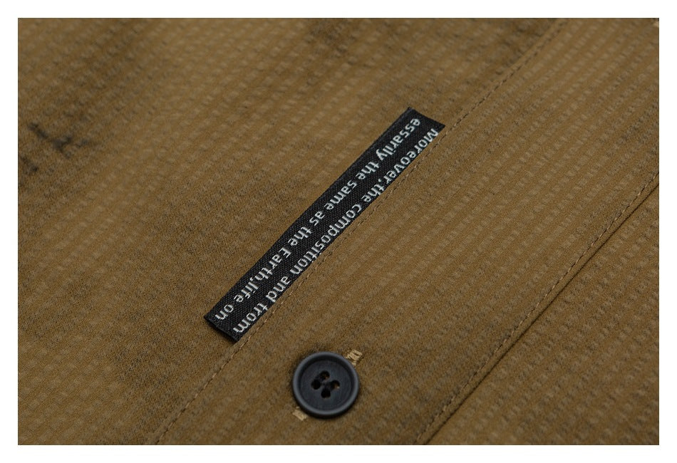 Close-up of a black English-text label and dark button on the brown textured shirt.