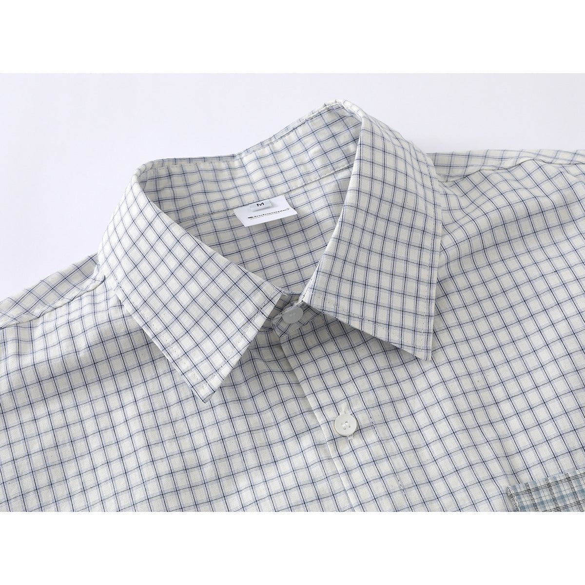 Close-up of a white shirt with a fine blue-gray check, pointed collar, white buttons and inner neck label.