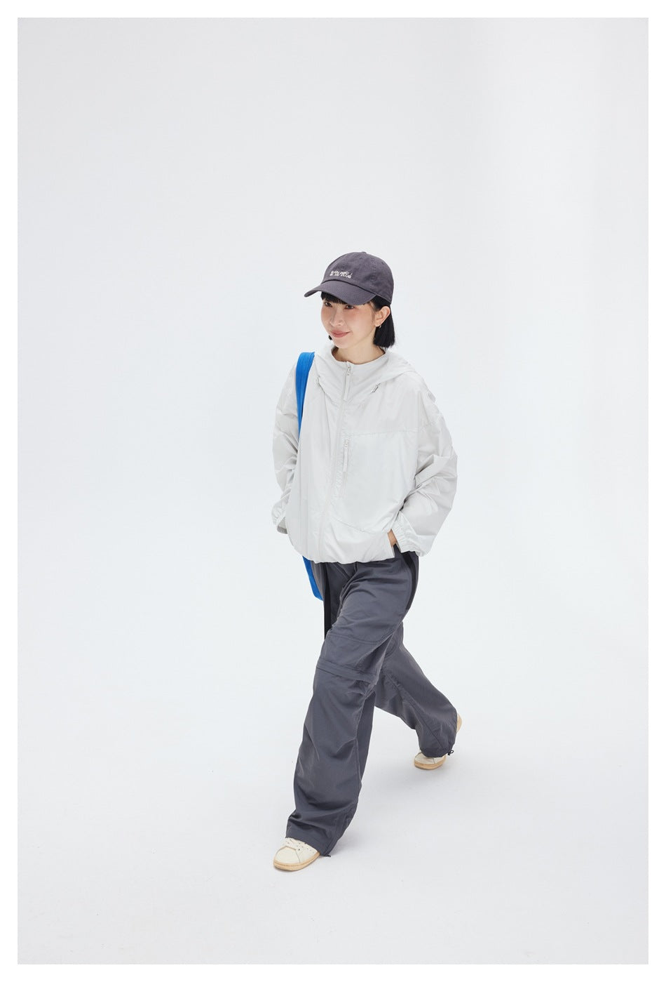 Model walking in a white hooded jacket and loose charcoal-gray trousers.