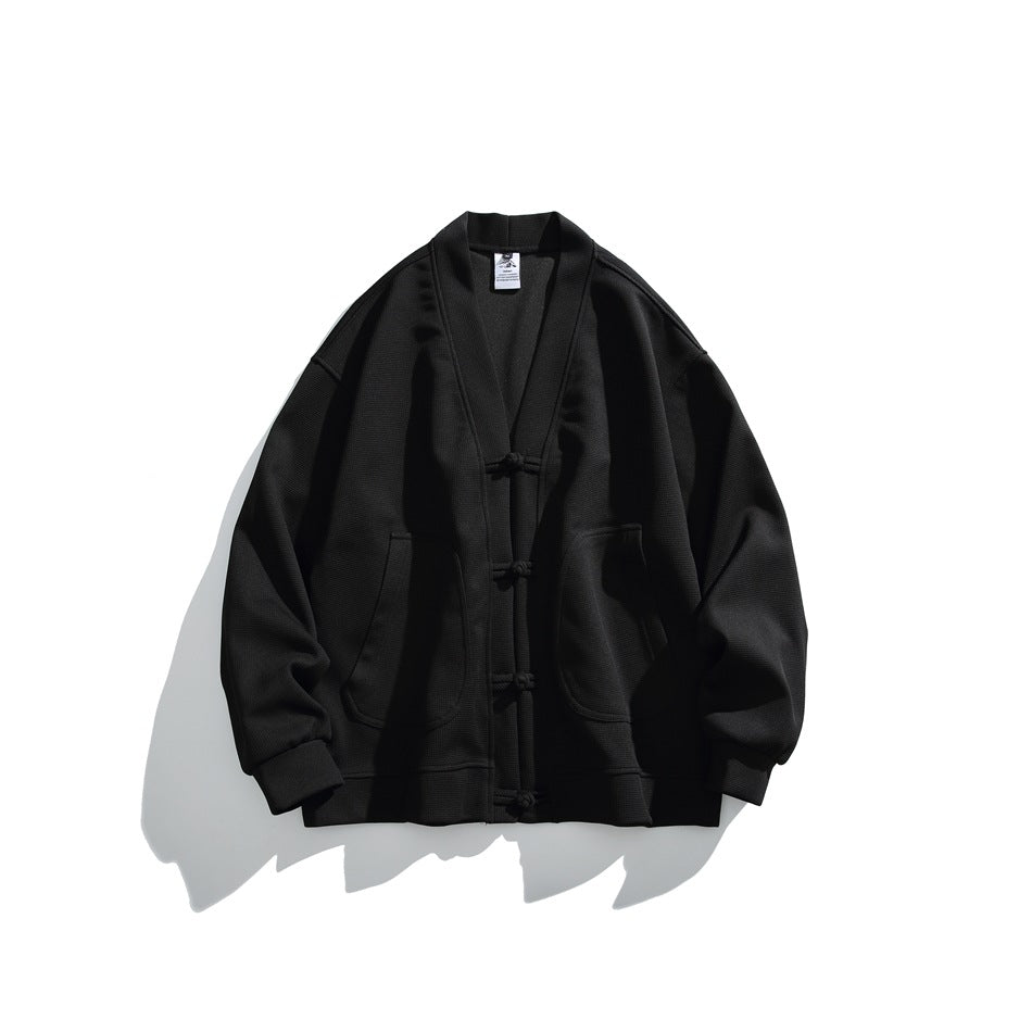 Black waffle-textured V-neck cardigan jacket with frog-button closures and rounded pockets, flat lay