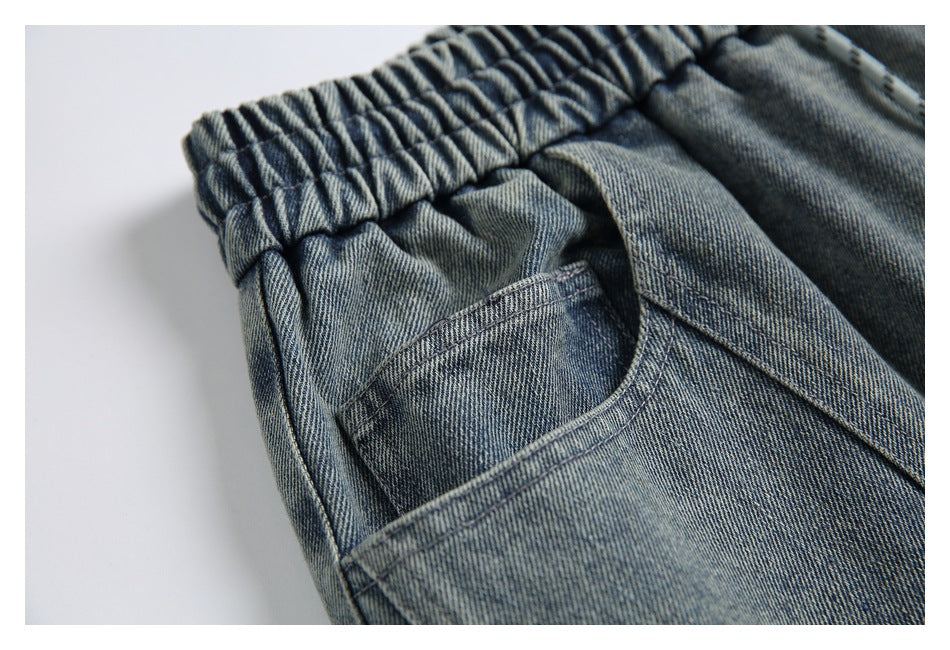 Close-up of faded blue denim pants showing the gathered elastic waistband and curved pocket opening.