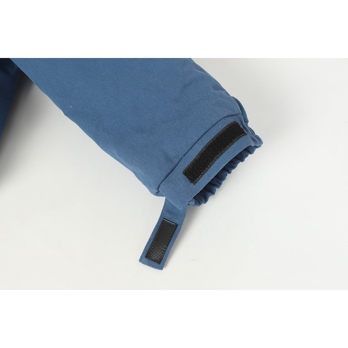 Close-up of a blue jacket sleeve cuff with an adjustable black hook-and-loop tab.