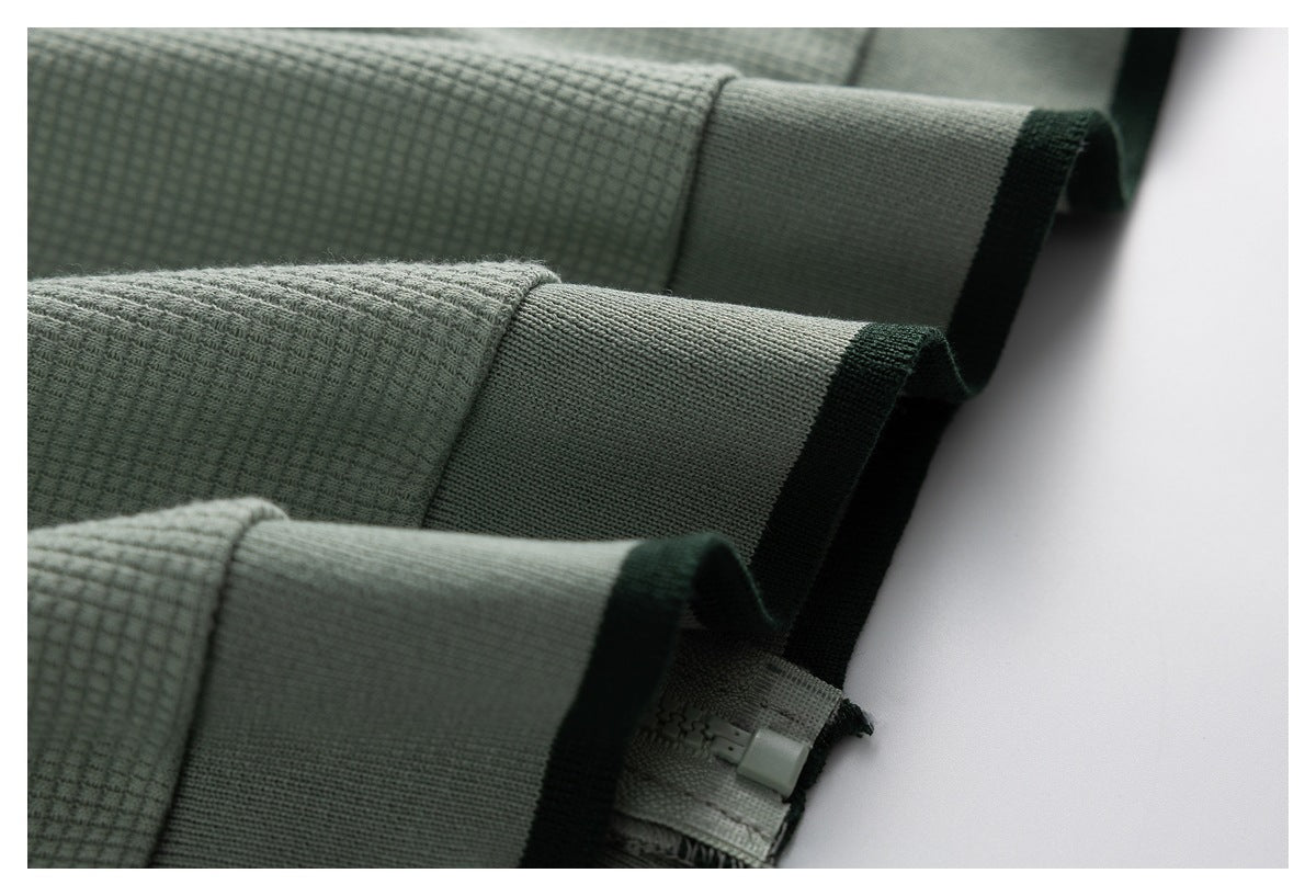 Close-up of folded sage green garment edges with dark green trim and a small interior tag.