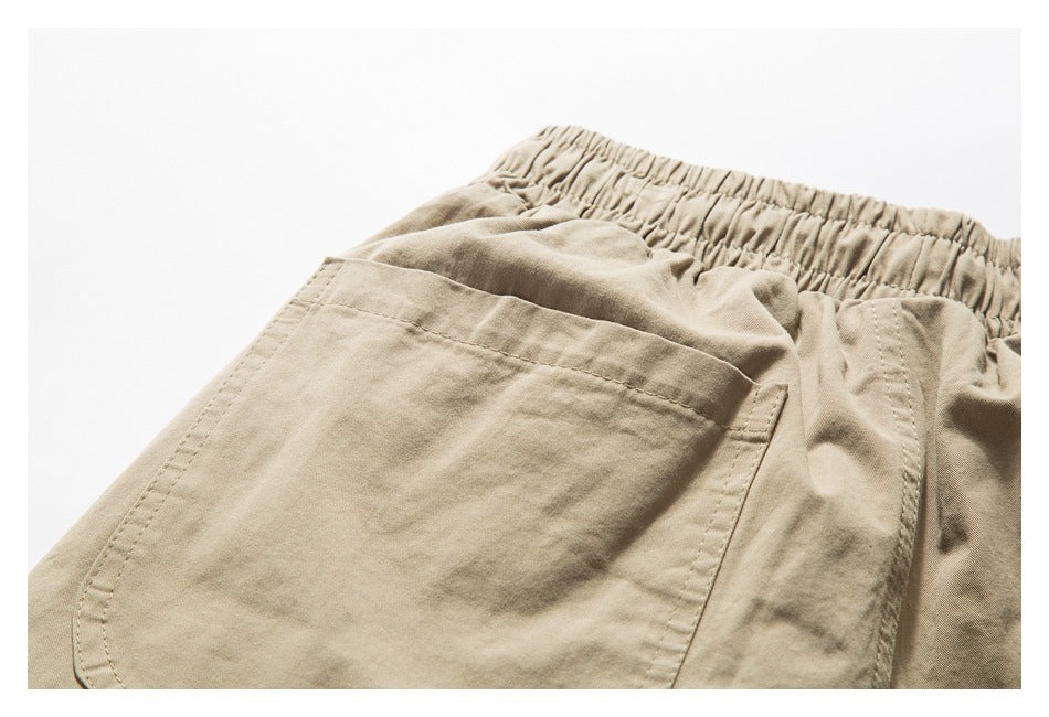 Close-up of beige shorts showing a large patch pocket, gathered waistband, and stitched seams.