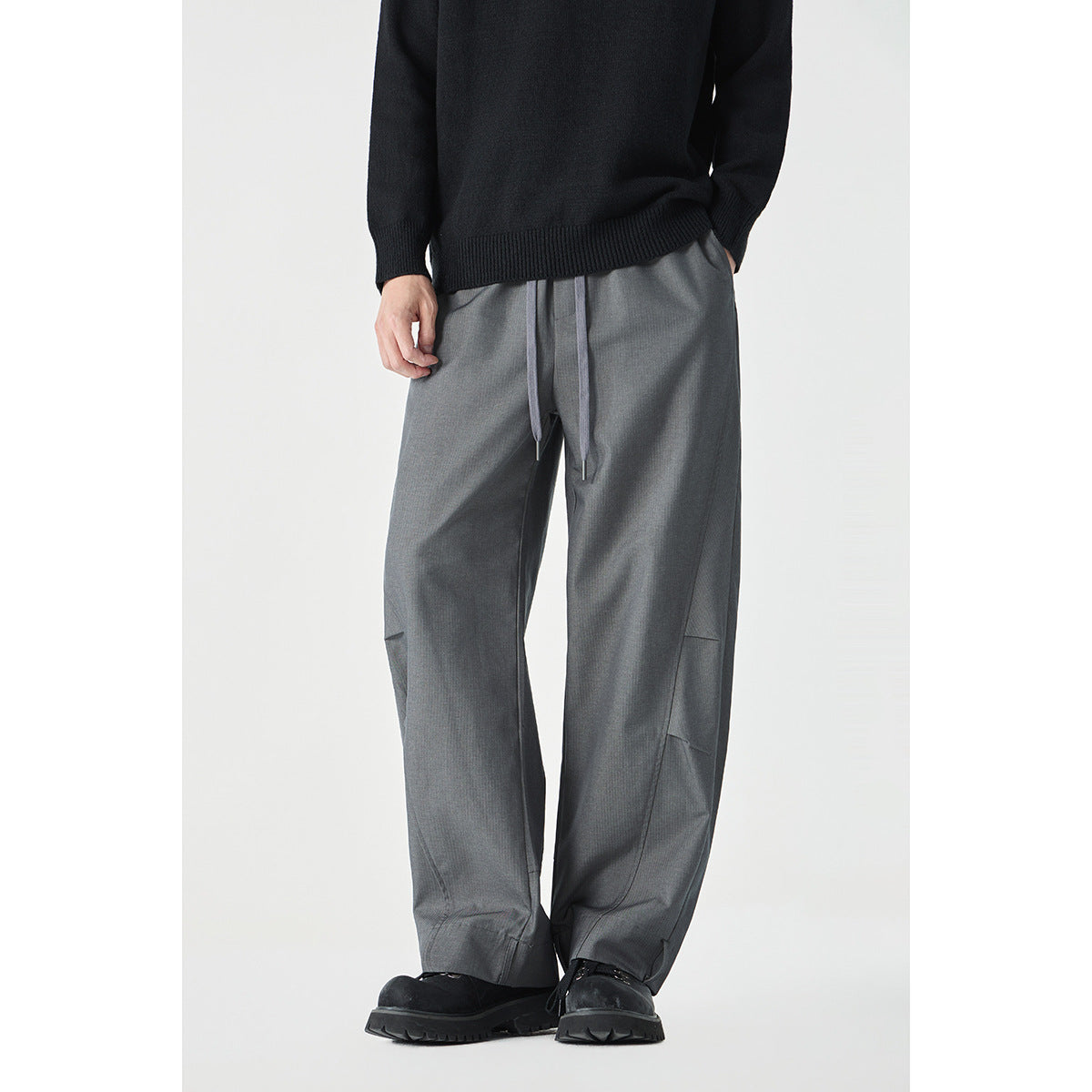 Model wearing loose gray drawstring pants with an elastic waist and wide legs, front view.