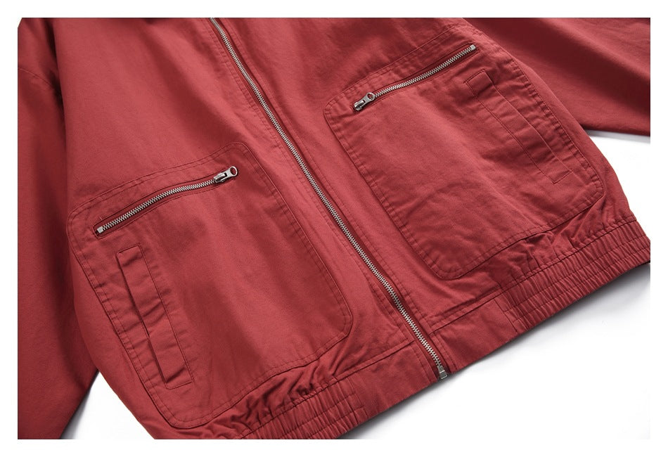 Close-up of a brick-red jacket front with a central zipper, two large zippered pockets, and an elasticized hem.