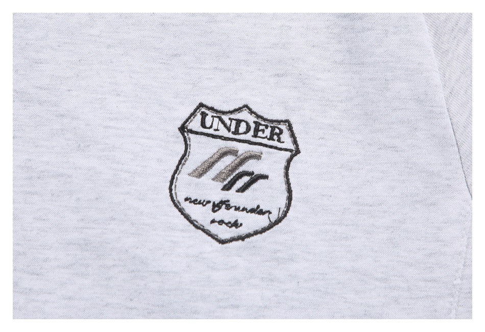 Close-up of a black embroidered shield emblem on the light gray sweatshirt.