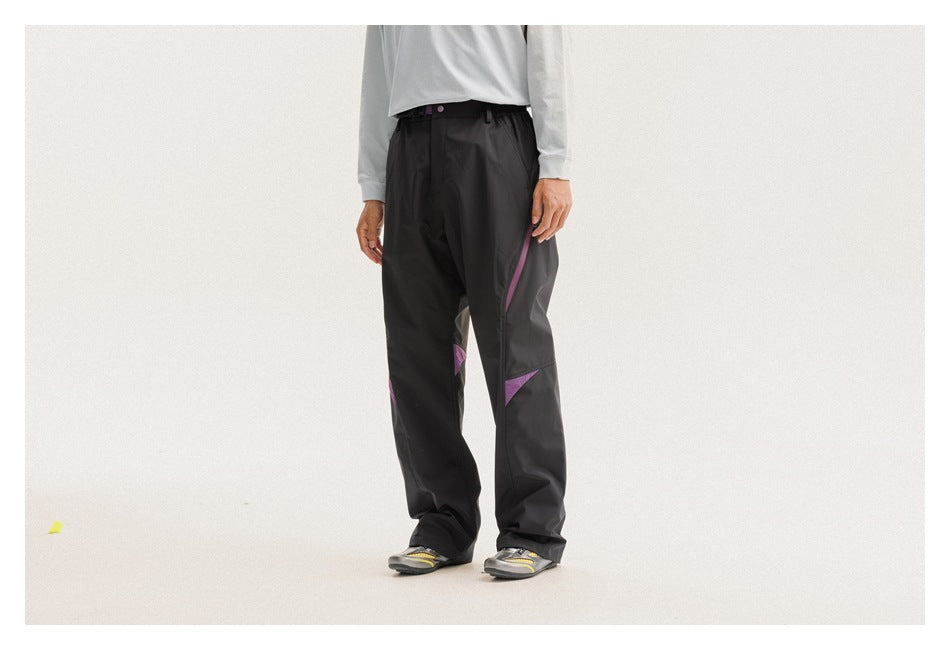 Front three-quarter view of a model wearing black trousers with purple zipper and knee accents.
